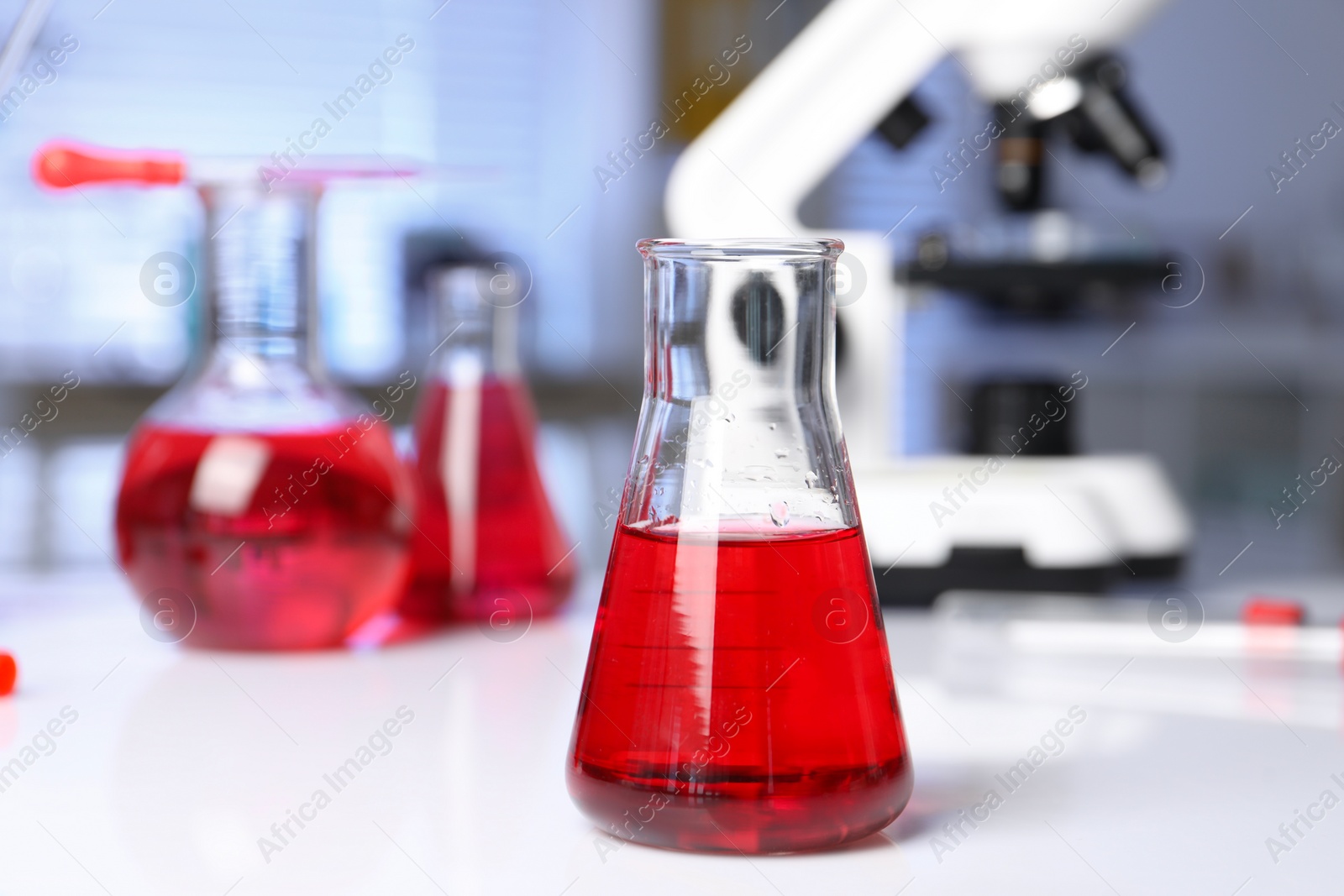 Photo of Laboratory analysis. Glass flask with red liquid and microscope on white table indoors