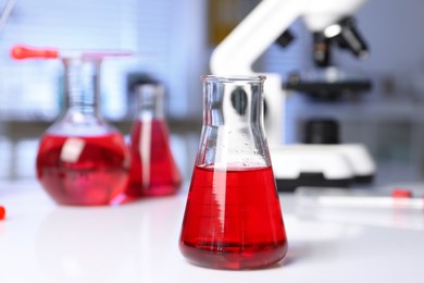 Laboratory analysis. Glass flask with red liquid and microscope on white table indoors