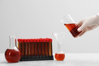 Photo of Scientist pouring liquid from beaker into conical flask on white table against light background, closeup