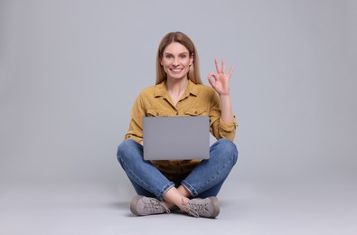 Photo of Happy woman with laptop showing ok gesture on light grey background