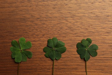 Photo of Green clover leaves on wooden background, flat lay. Space for text