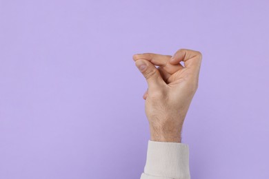 Photo of Man snapping fingers on violet background, closeup of hand. Space for text
