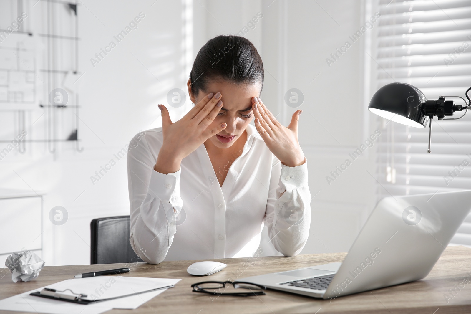 Photo of Stressed and tired young woman with headache at workplace