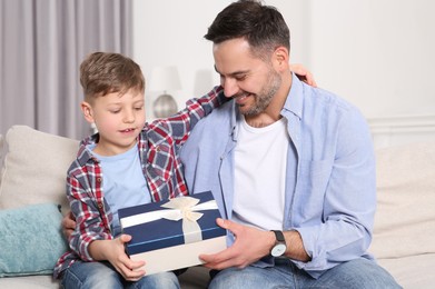 Photo of Cute little boy presenting his father with gift on sofa at home