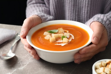 Woman with bowl of tasty sweet potato soup at table, closeup