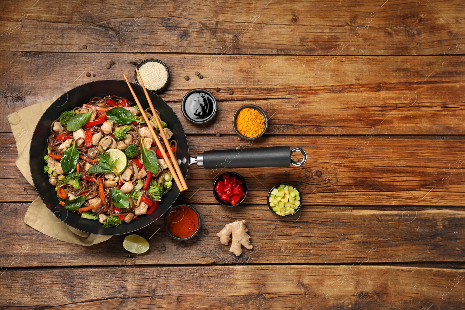 Photo of Stir-fry. Tasty noodles with meat in wok, chopsticks and ingredients on wooden table, flat lay. Space for text