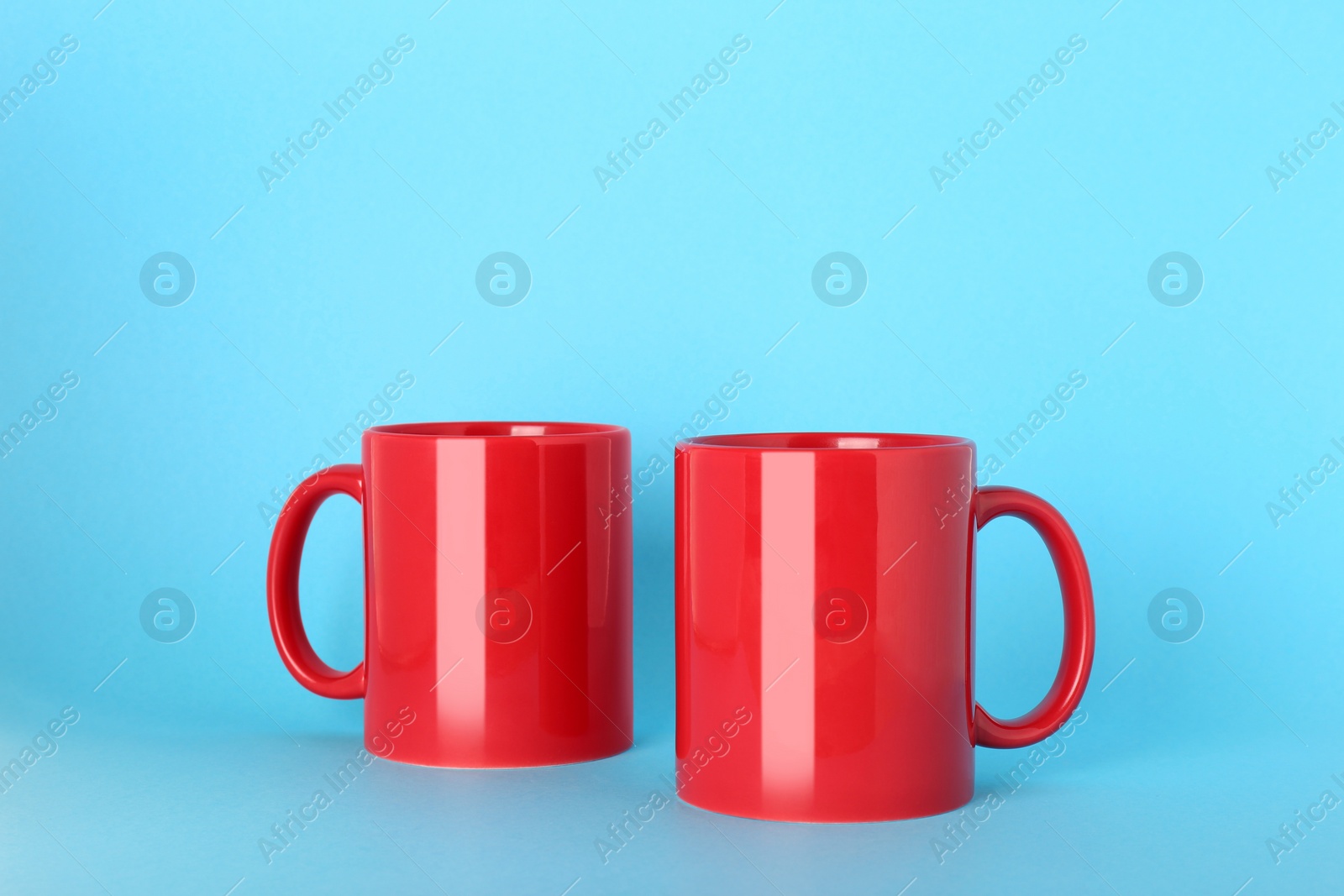 Blank red ceramic mugs on light blue background Photo of Blank red ceramic mugs on light blue background