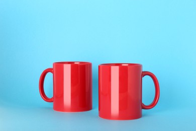 Photo of Blank red ceramic mugs on light blue background