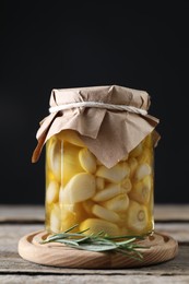 Photo of Garlic with honey in glass jar and rosemary on wooden table against black background