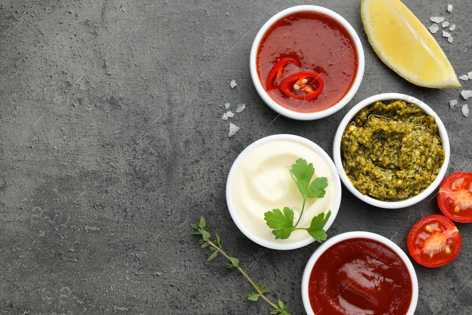 Photo of Different tasty sauces in bowls and ingredients on grey table, flat lay. Space for text