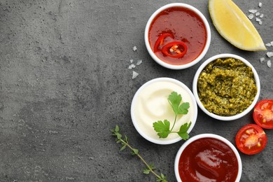 Different tasty sauces in bowls and ingredients on grey table, flat lay. Space for text