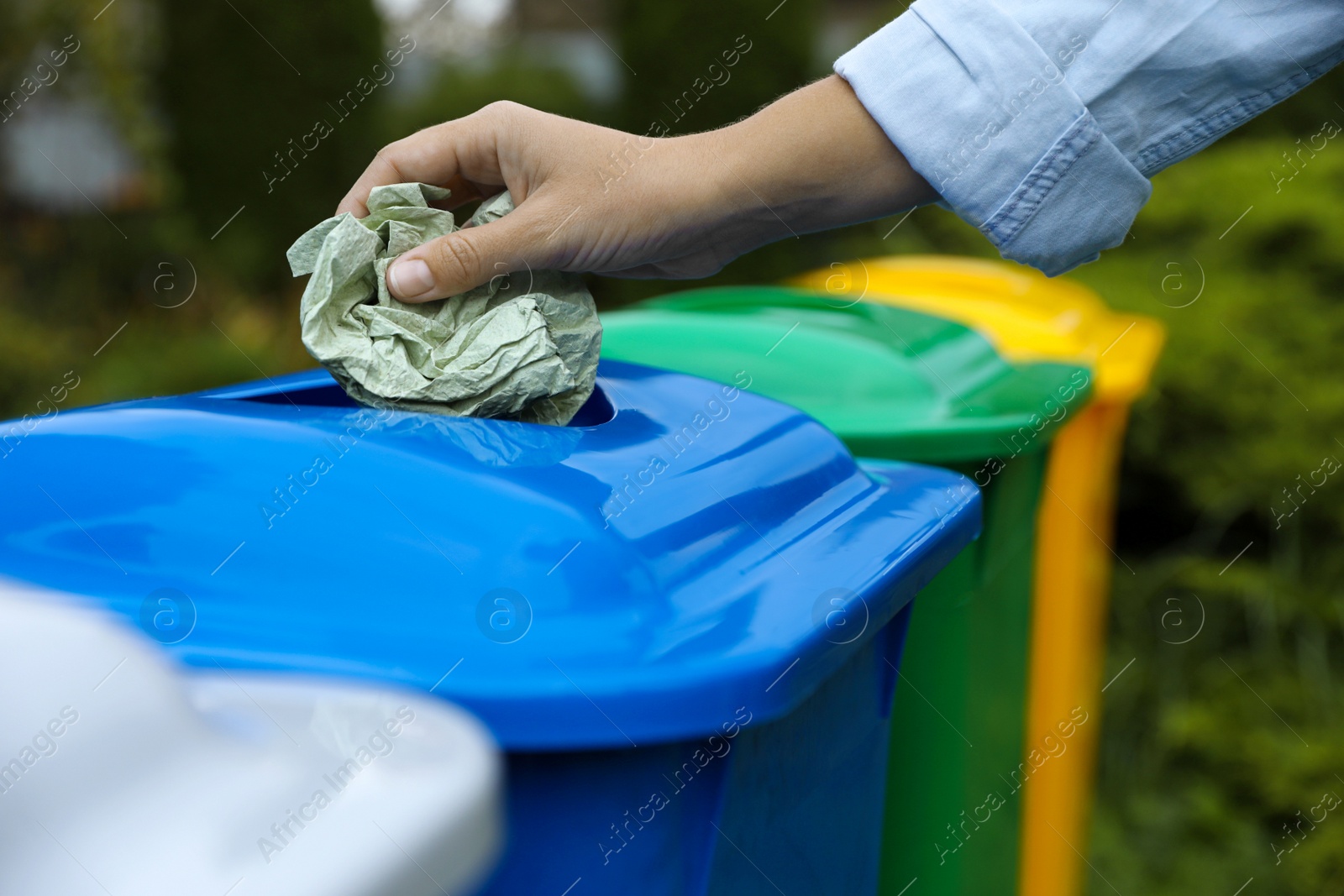 Photo of Woman throwing crumpled tissue into recycling bin outdoors, closeup