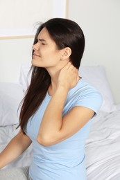 Photo of Young woman suffering from neck pain on bed in bedroom