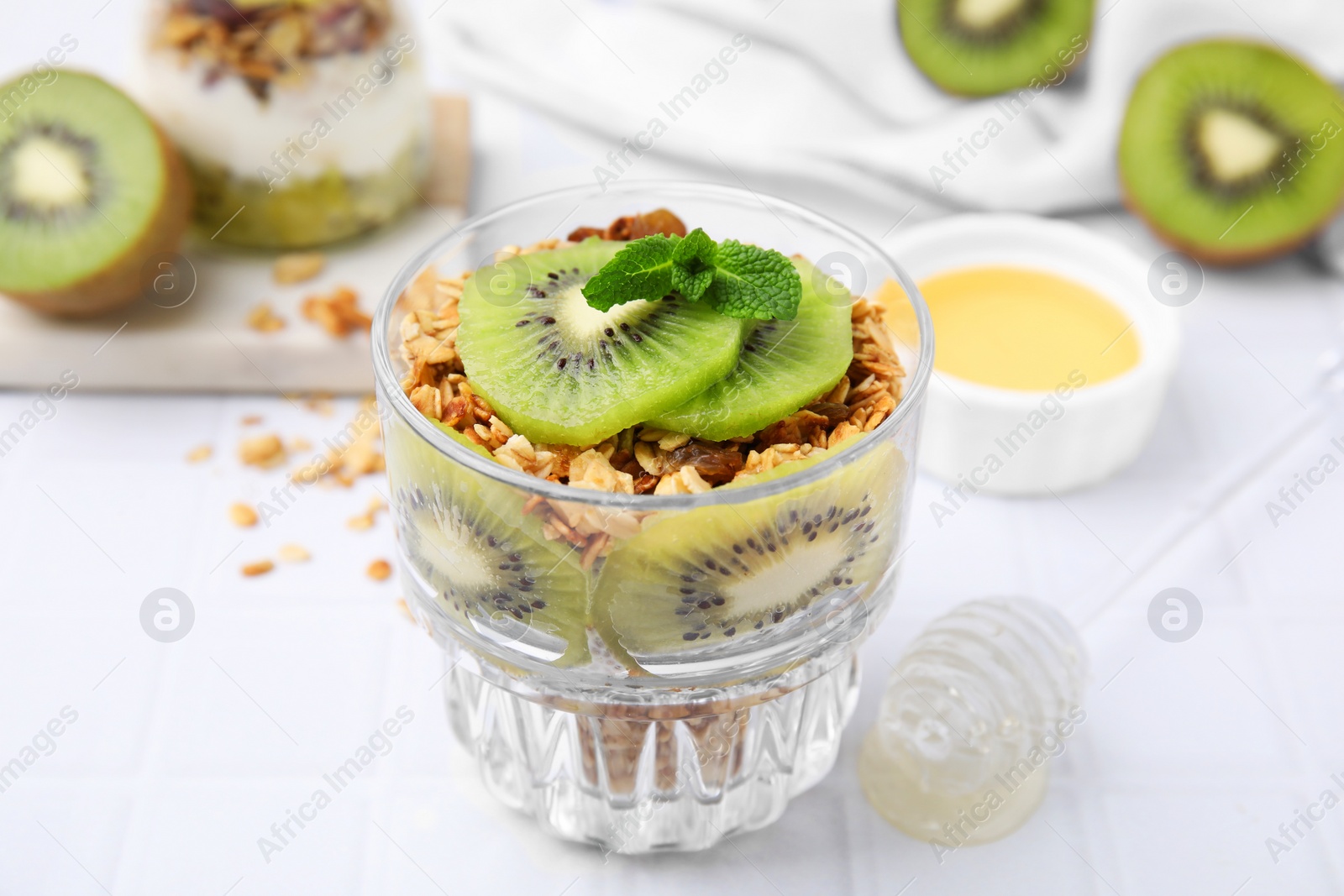 Photo of Delicious dessert with kiwi and muesli on white table, closeup