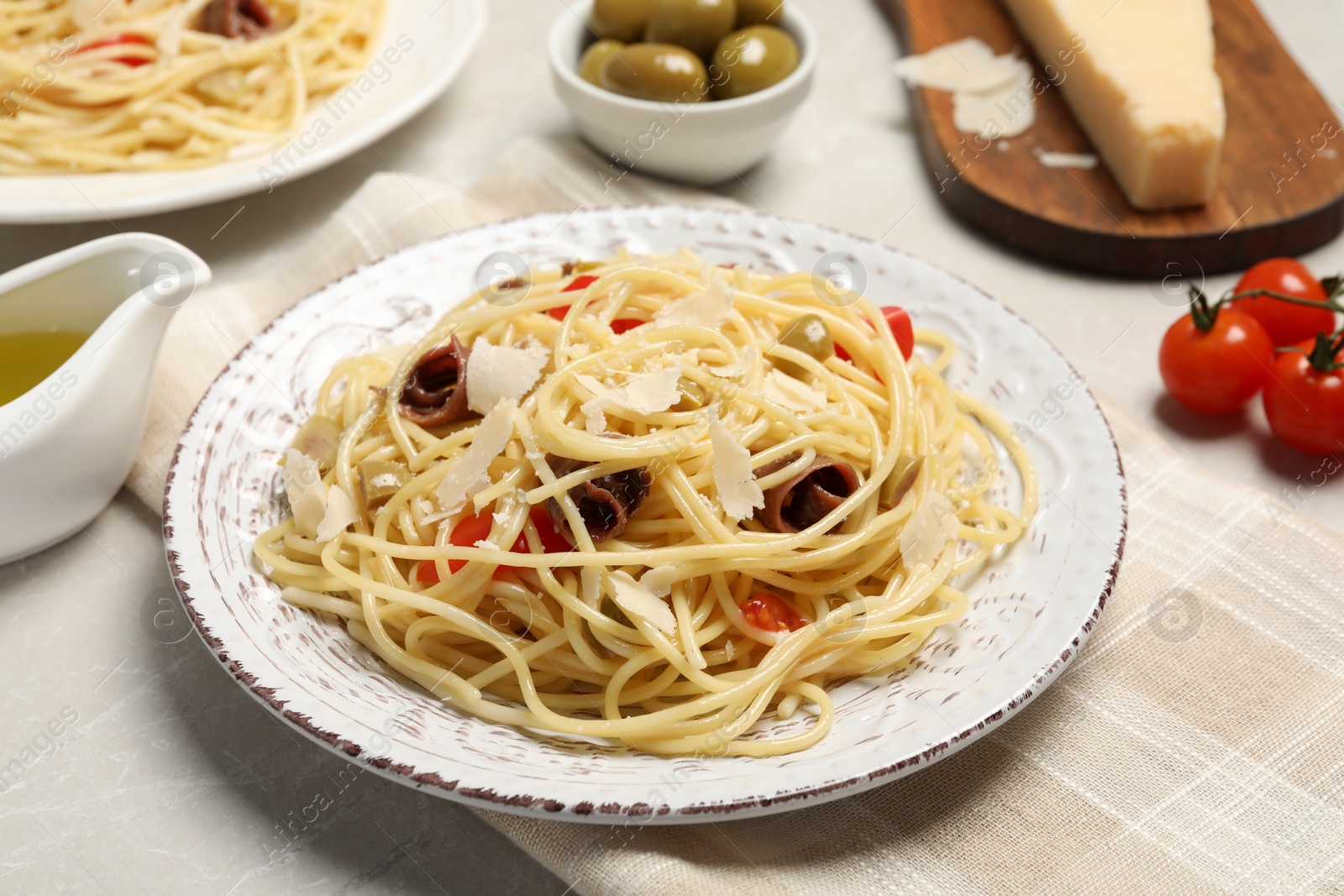 Photo of Delicious pasta with anchovies, tomatoes and parmesan cheese on light grey table