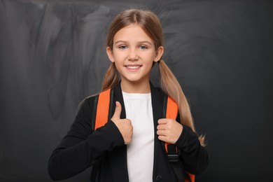 Photo of Smiling schoolgirl showing thumb up near blackboard
