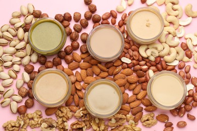Different types of delicious nut butters and ingredients on pink background, flat lay