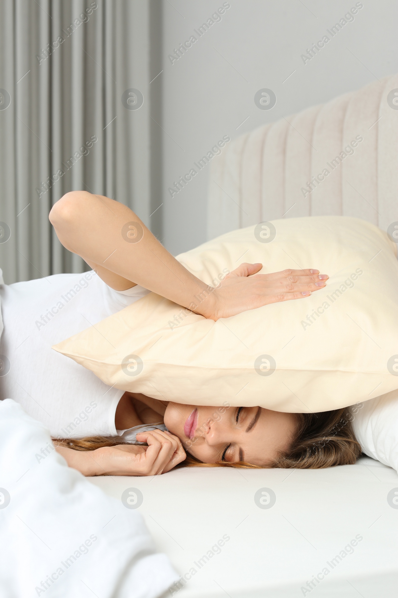 Photo of Sleepless woman covering head with pillow in bed at home