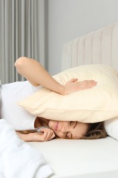 Photo of Sleepless woman covering head with pillow in bed at home