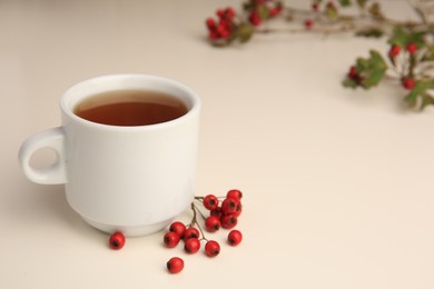 Aromatic hawthorn tea in cup and berries on beige table, closeup. Space for text