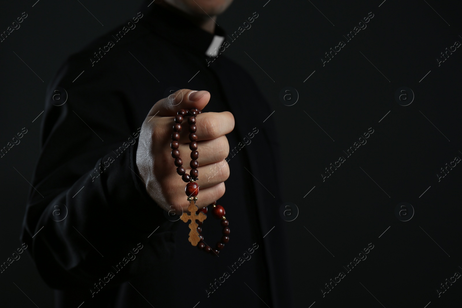 Photo of Priest with rosary beads on black background, closeup. Space for text