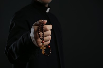 Photo of Priest with rosary beads on black background, closeup. Space for text