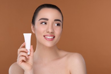 Woman holding tube of foundation on brown background