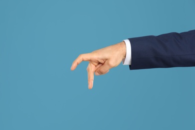 Photo of Businessman imitating walk with hand on light blue background, closeup. Finger gesture