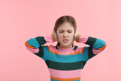 Hearing problem. Little girl suffering from ear pain on pink background