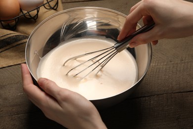 Photo of Woman whipping ingredients with balloon whisk at wooden table, closeup. Cooking delicious eggnog