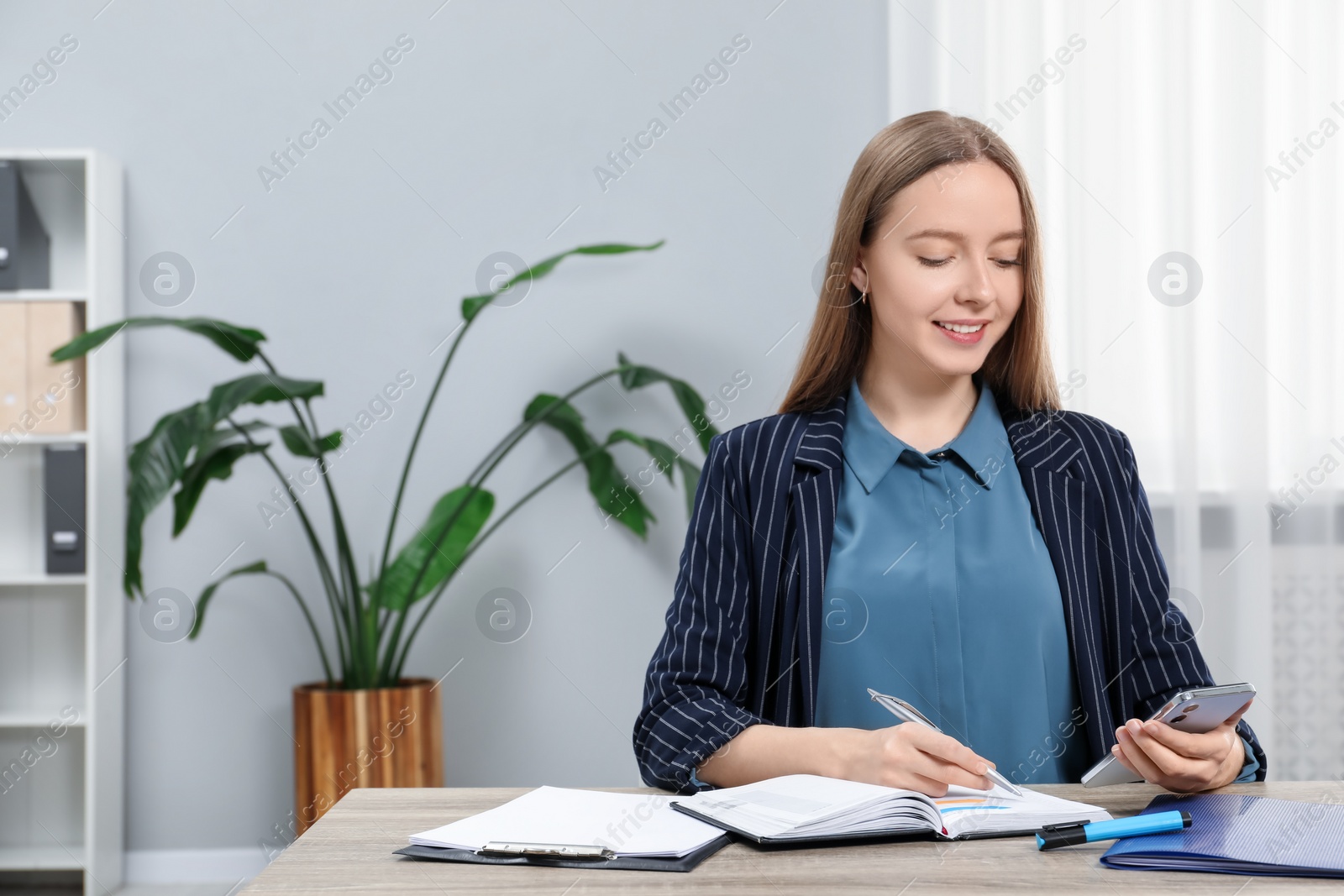 Photo of Woman taking notes while using smartphone at wooden table in office, space for text