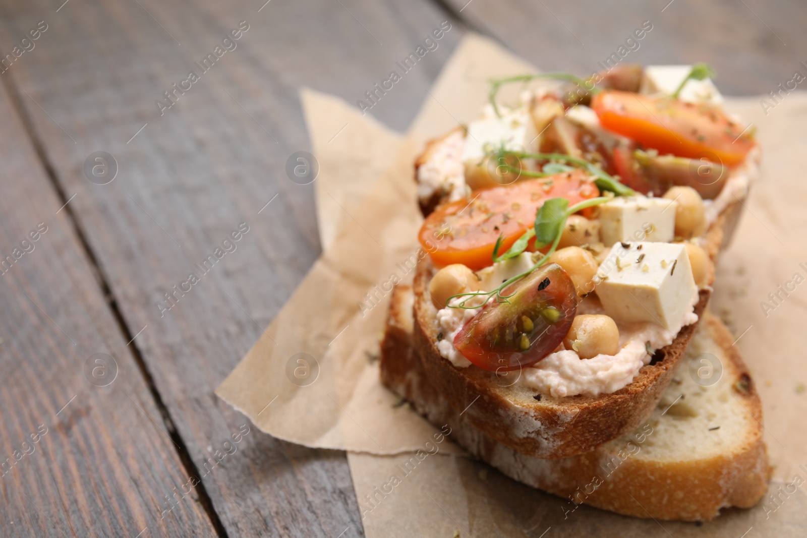 Photo of Tasty vegan sandwich with tomatoes, tofu and chickpeas on wooden table, closeup. Space for text