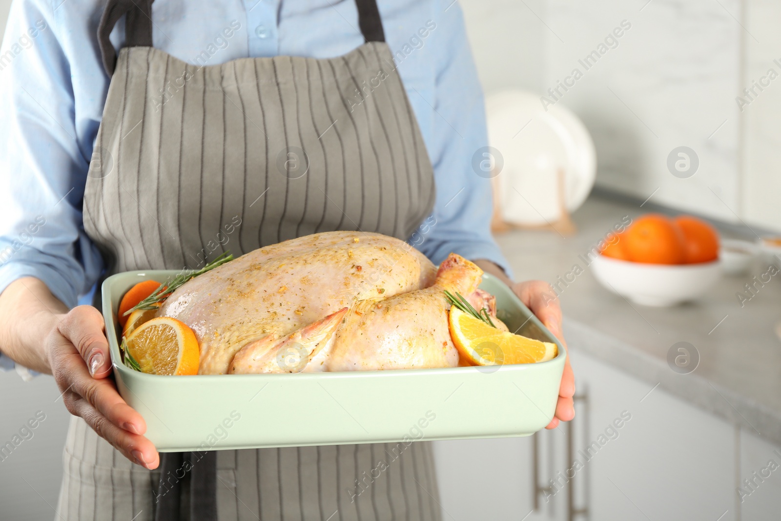 Photo of Woman holding pan with raw chicken and oranges in kitchen, closeup