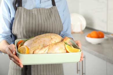 Woman holding pan with raw chicken and oranges in kitchen, closeup