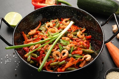 Photo of Shrimp stir fry with vegetables in wok and ingredients on black table