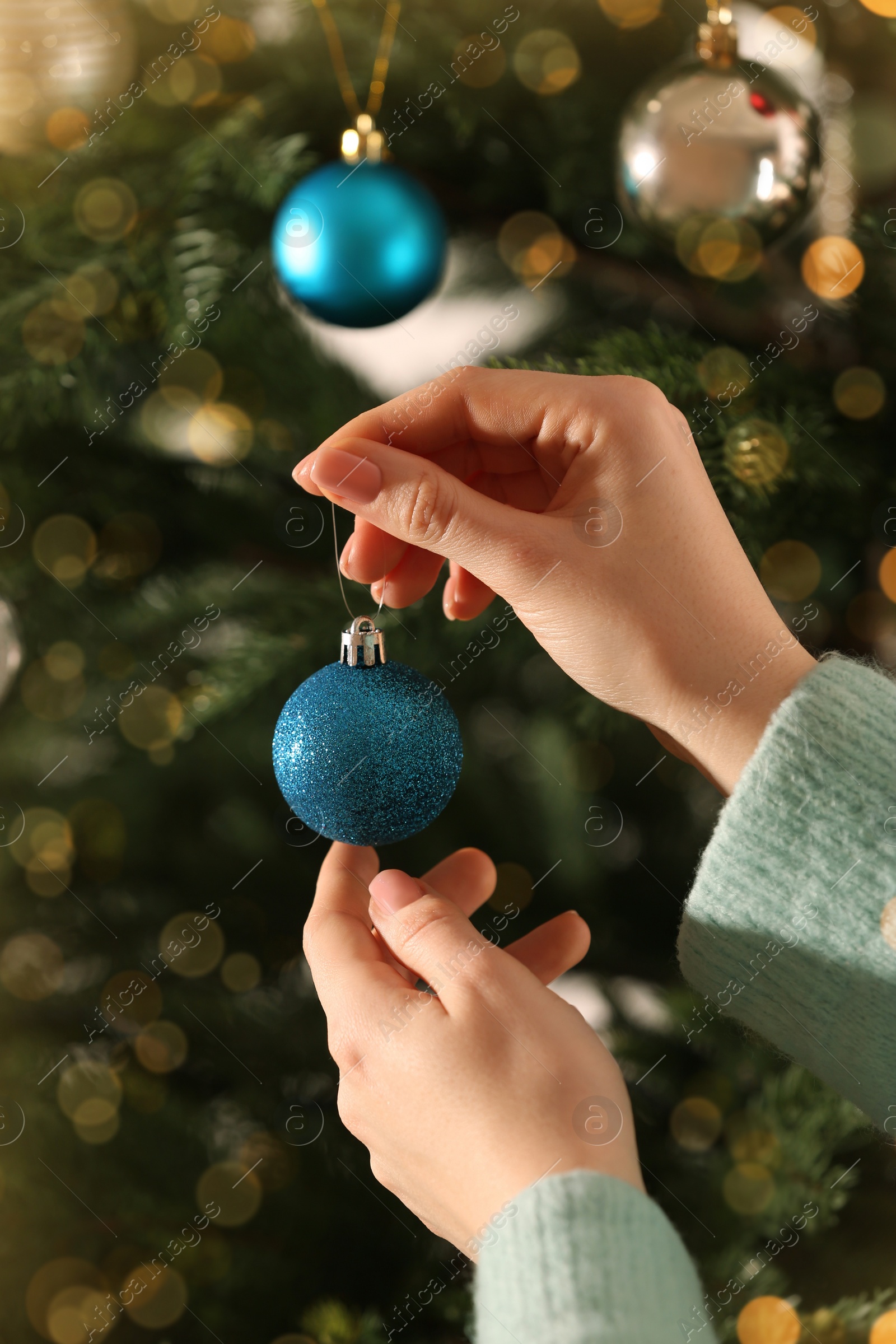 Photo of Woman holding beautiful light blue bauble near Christmas tree indoors, closeup