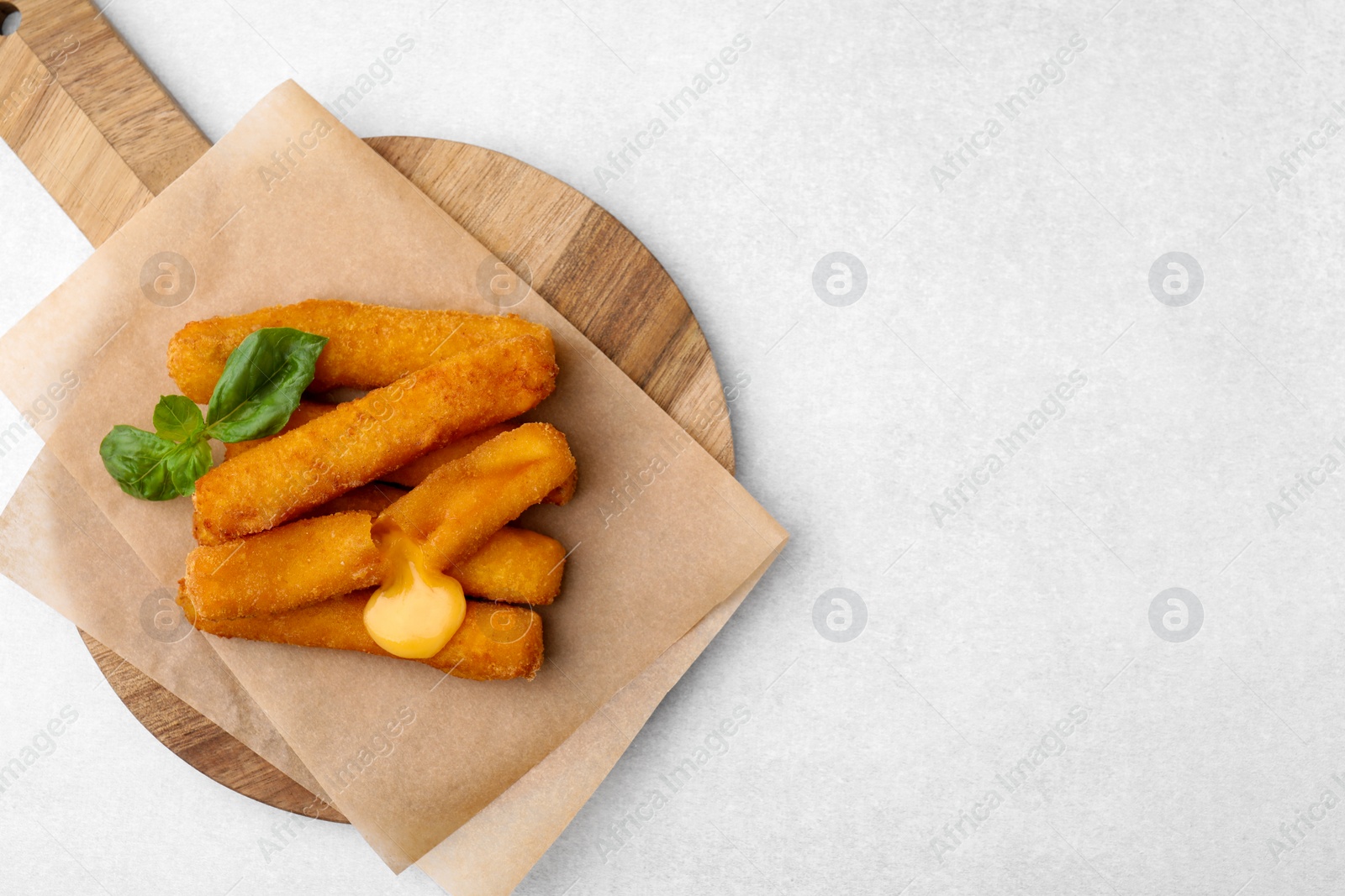 Photo of Tasty fried mozzarella sticks and basil on light table, top view. Space for text