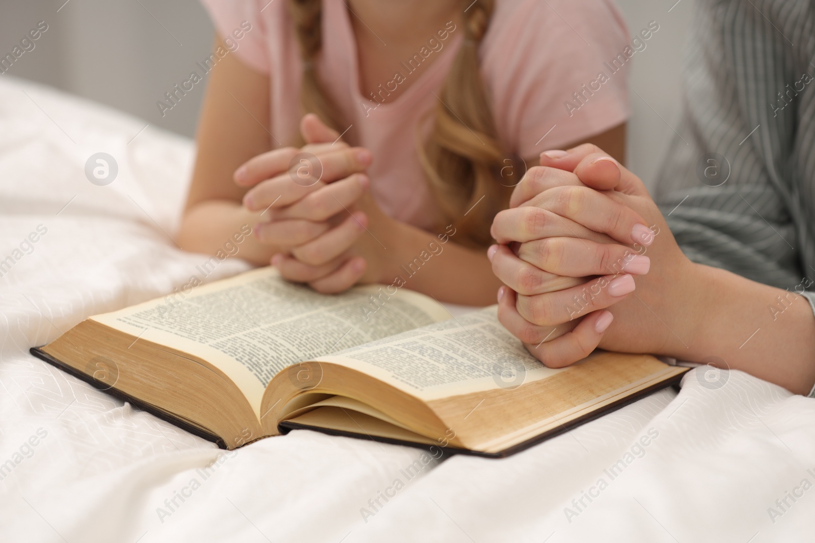 Photo of Girl and her godparent praying over Bible together indoors, closeup