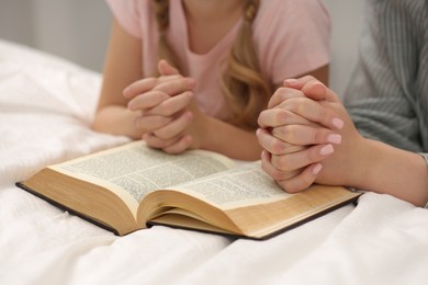 Girl and her godparent praying over Bible together indoors, closeup