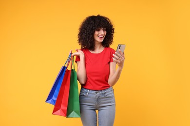 Photo of Happy young woman with shopping bags and modern smartphone on yellow background