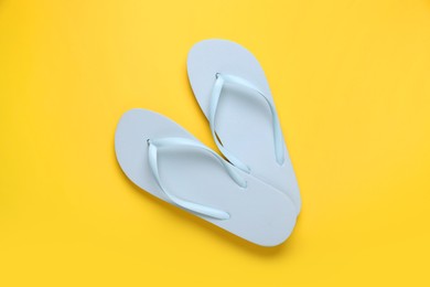 Stylish white flip flops on yellow background, top view