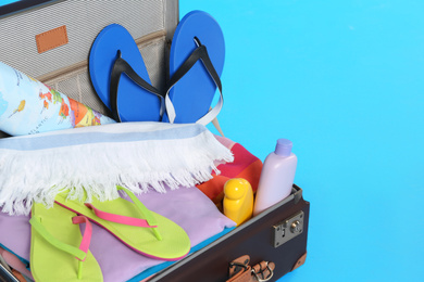 Photo of Open vintage suitcase with different beach objects packed for summer vacation on light blue background, closeup