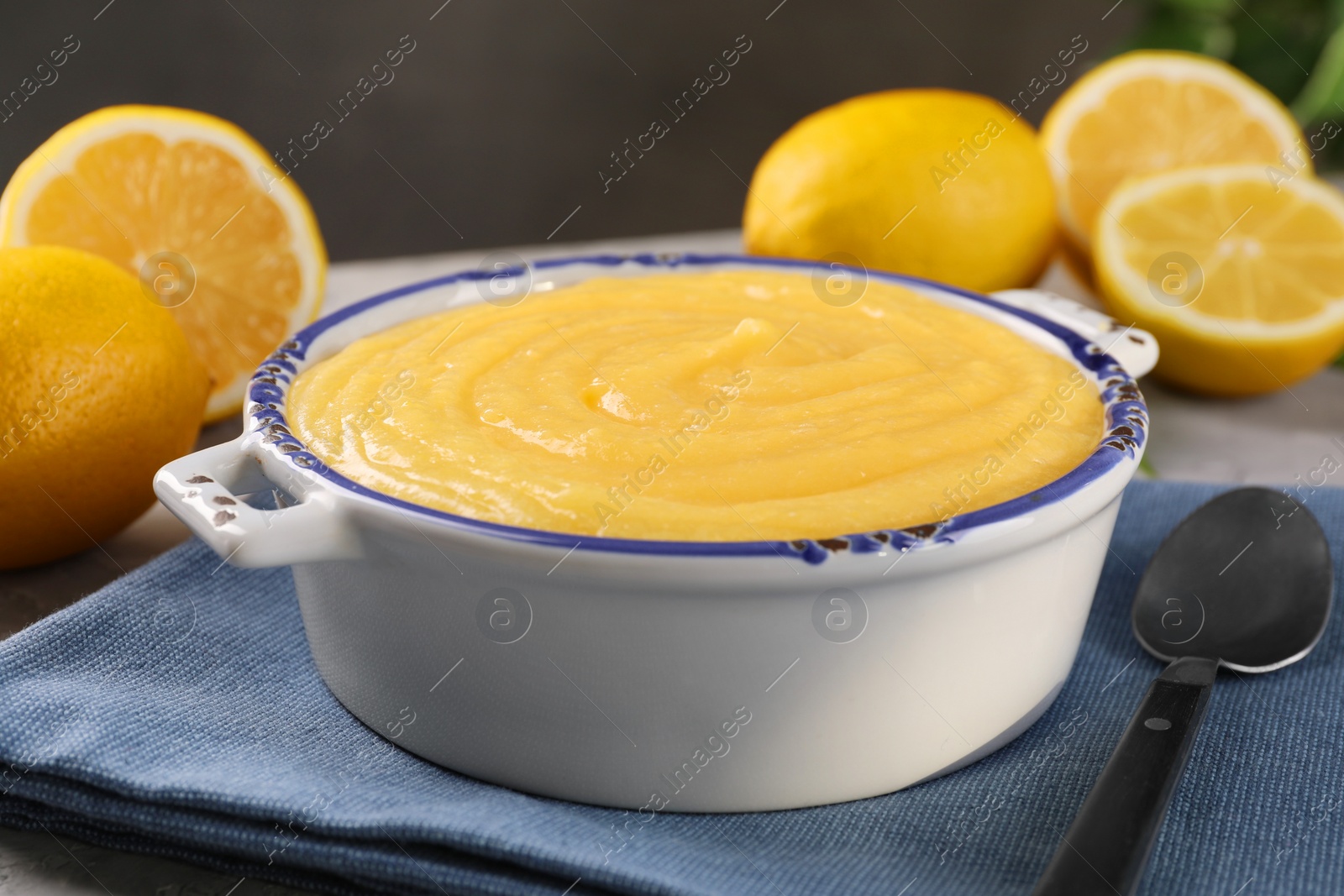 Photo of Delicious lemon curd in bowl, fresh citrus fruits and spoon on table, closeup