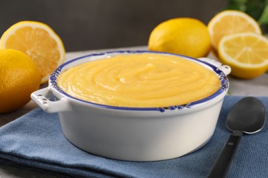 Delicious lemon curd in bowl, fresh citrus fruits and spoon on table, closeup