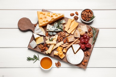 Cheese plate with honey, grapes and nuts on white wooden table, top view