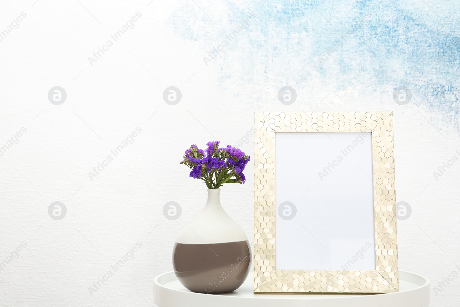 Photo of Blank frame and vase with flowers on table near light wall. Mock up for design