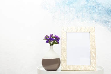 Photo of Blank frame and vase with flowers on table near light wall. Mock up for design