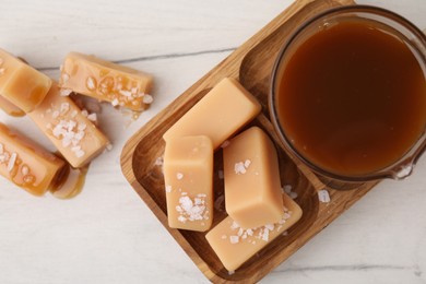 Yummy caramel candies, sauce and sea salt on white wooden table, top view