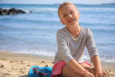 Photo of Happy little girl on sandy beach near sea. Space for text