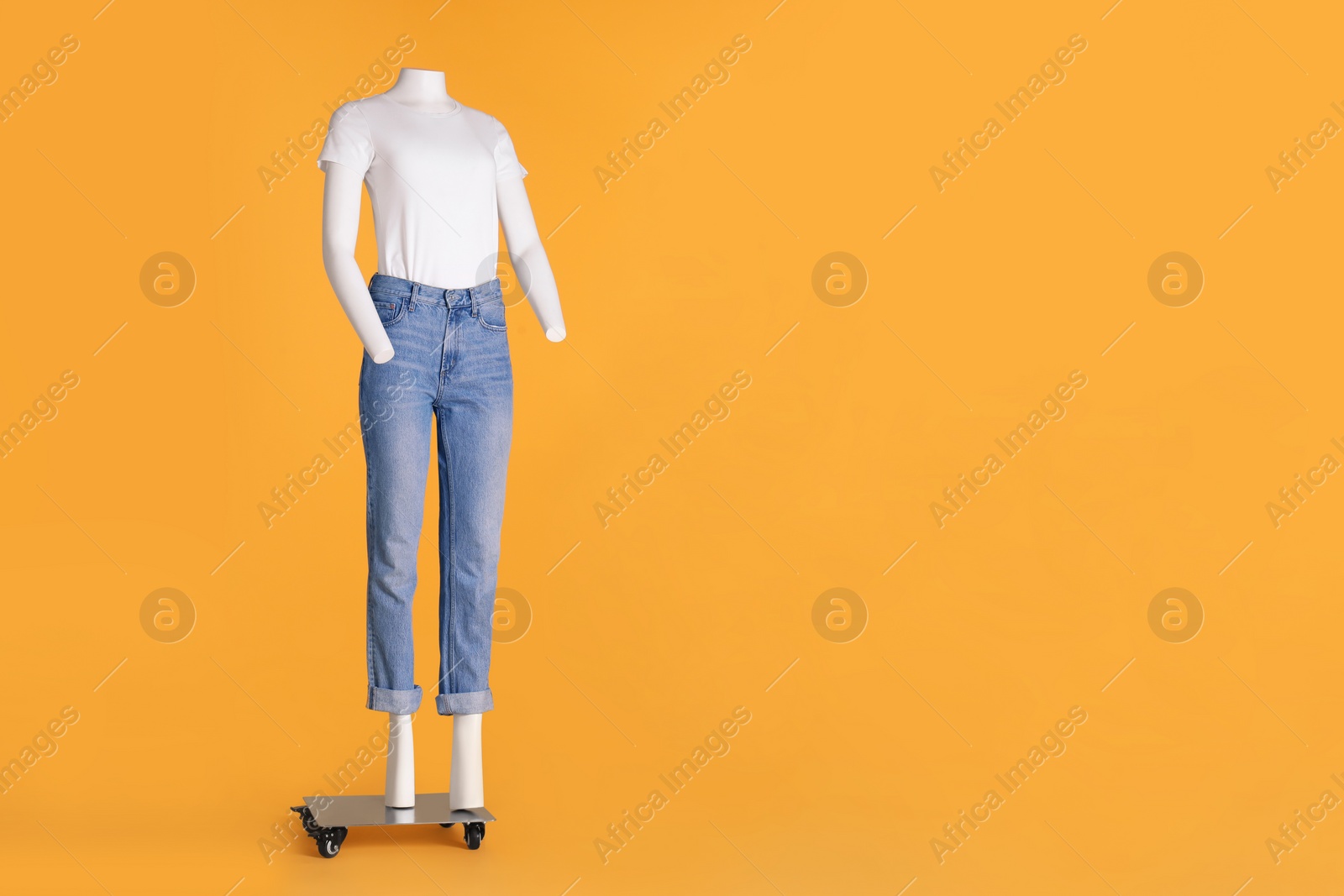 Photo of Female mannequin dressed in white t-shirt and stylish jeans on orange background, space for text